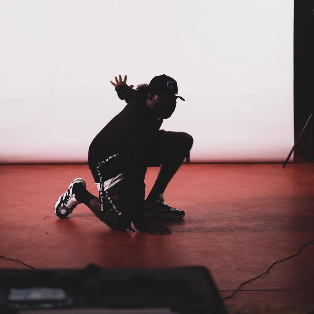 Artist wearing a mask crouching in front of a paper backdrop
