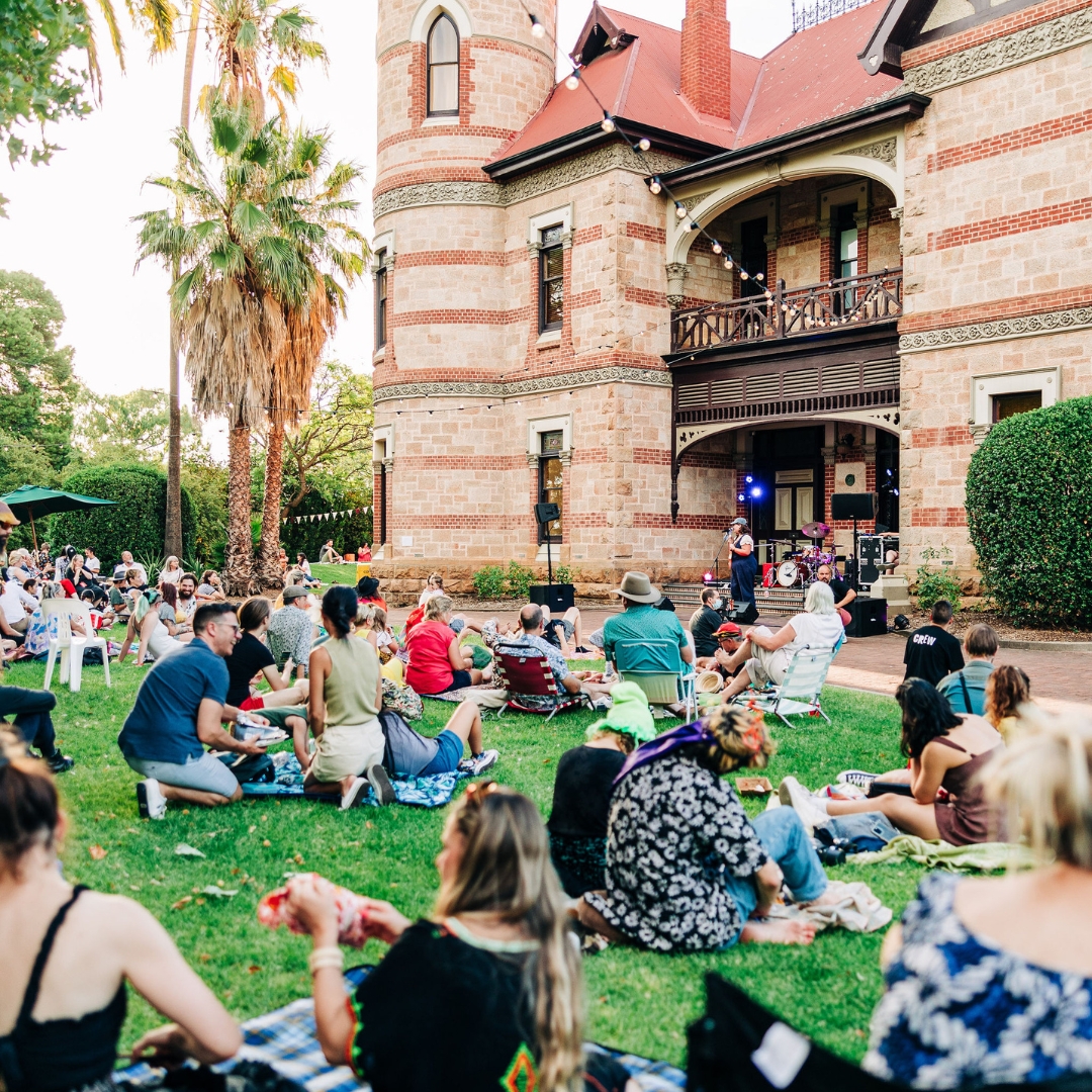 People sitting on picnic blankets watching a performance in front of Carclew House